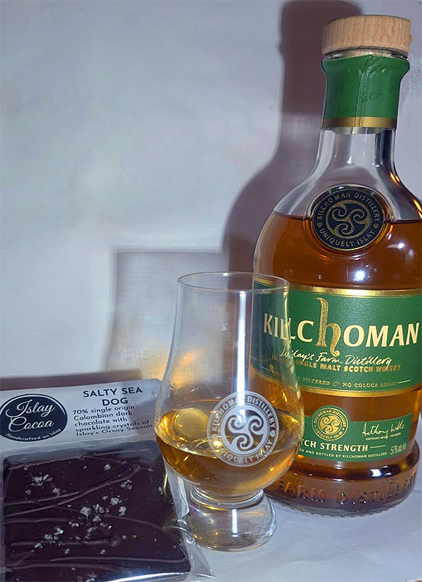 Picture of a bottle of Kilchoman Batch Strength Islay single malt whisky with a dram next to it. Next to it some Salty Sea Dog Islay Cocoa chocolate